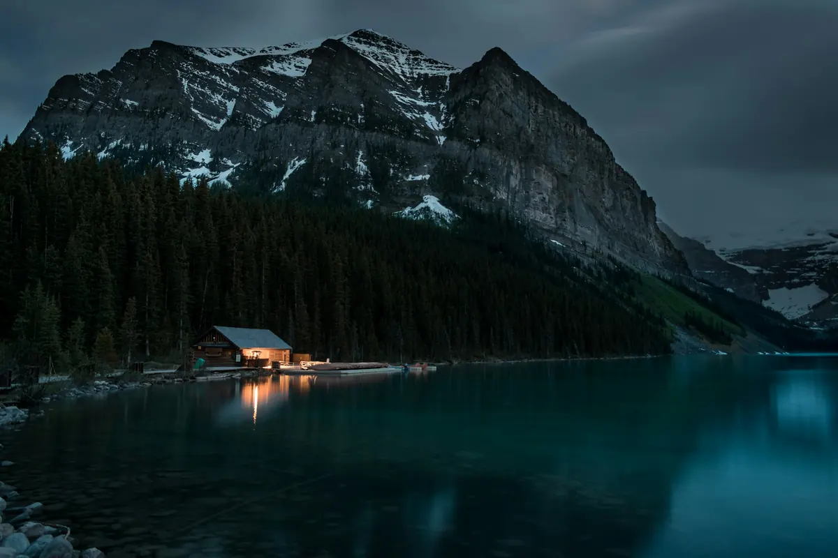 Wooden cabin on a lake with mountains behind it, morning light